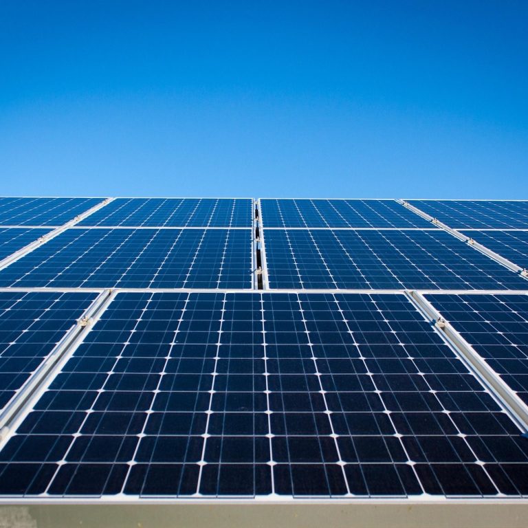 Reihe von Photovoltaik-Solarmodulen auf einer Fläche installiert, aufgenommen bei klarem Himmel.
