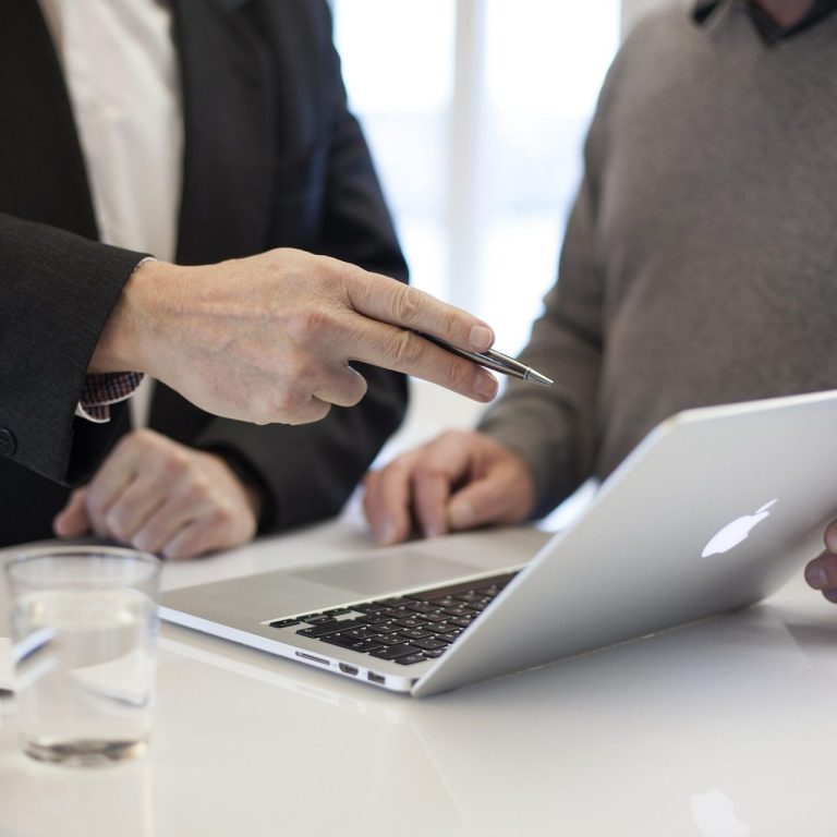 Zwei Personen besprechen Inhalte an einem geöffneten Laptop, eine Person zeigt mit einem Stift auf den Bildschirm während die andere bedient